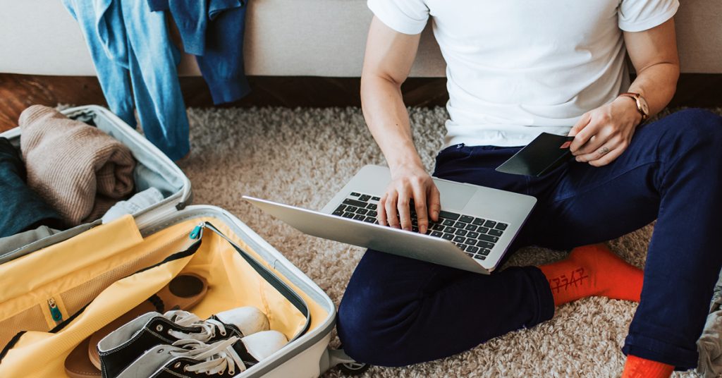 Man checking laptop in front of a suitcase
